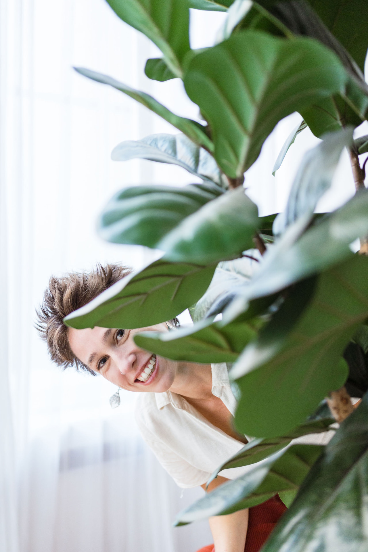 Silke kijkt lachend tussen groene bladeren door